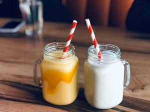 Tasty mango and vanilla smoothies in mason jars with striped straws on wooden table.