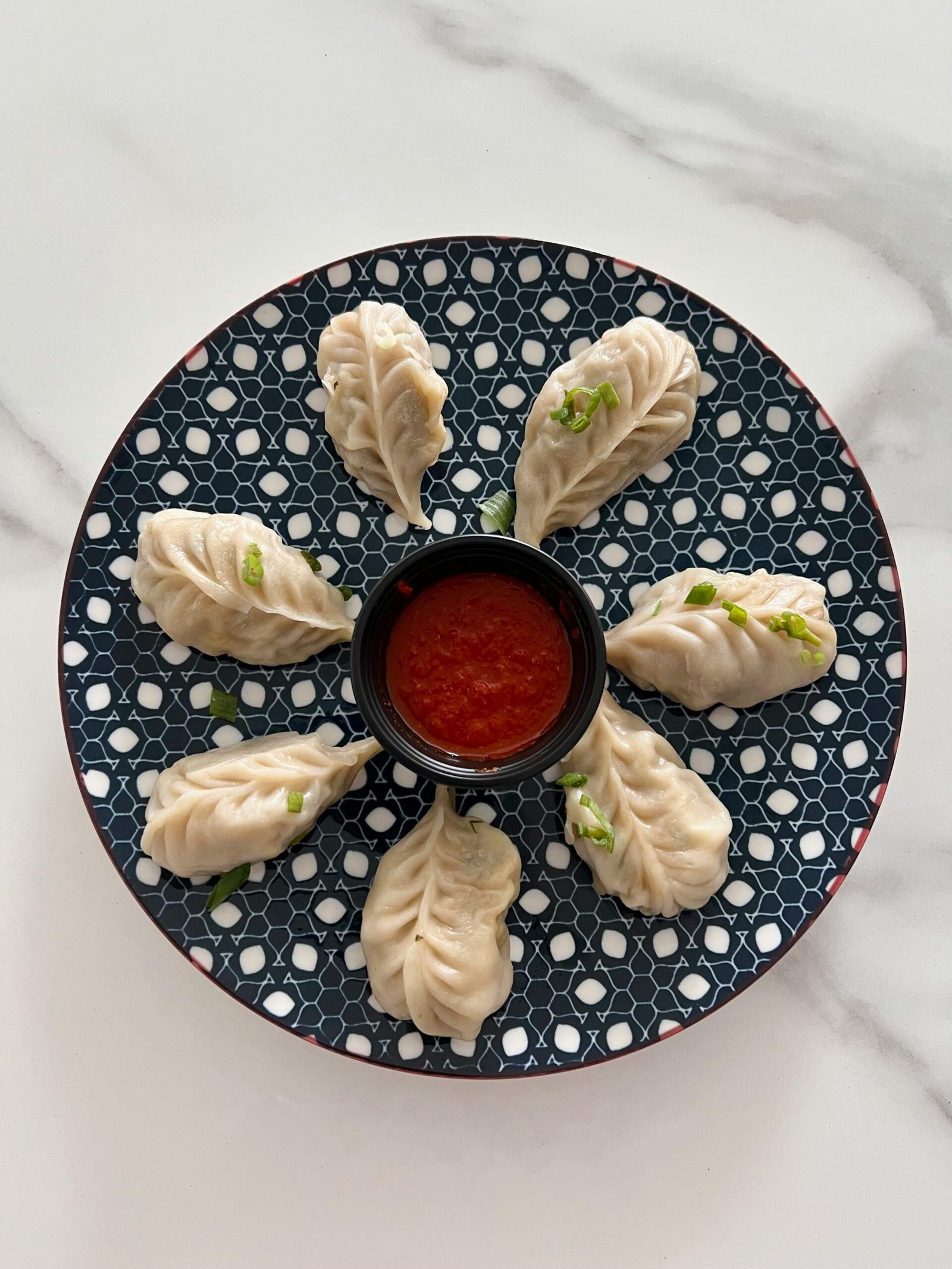 Delicious handmade momos served with spicy dipping sauce on a patterned plate.